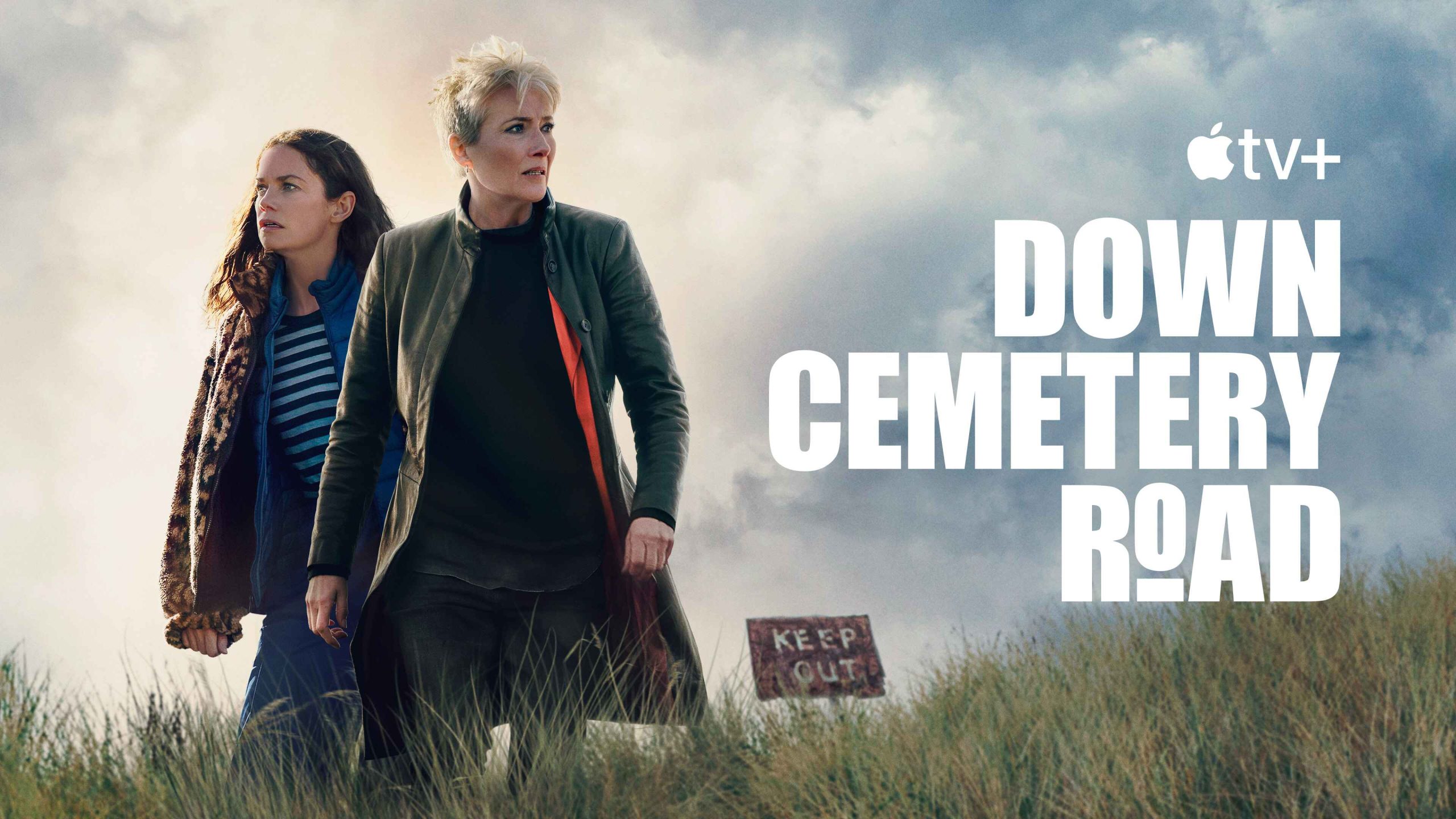Down Cemetery Road tanıtım görselinde kırlık alanda yürüyen iki kadın ve yanlarında Keep Out tabelası.