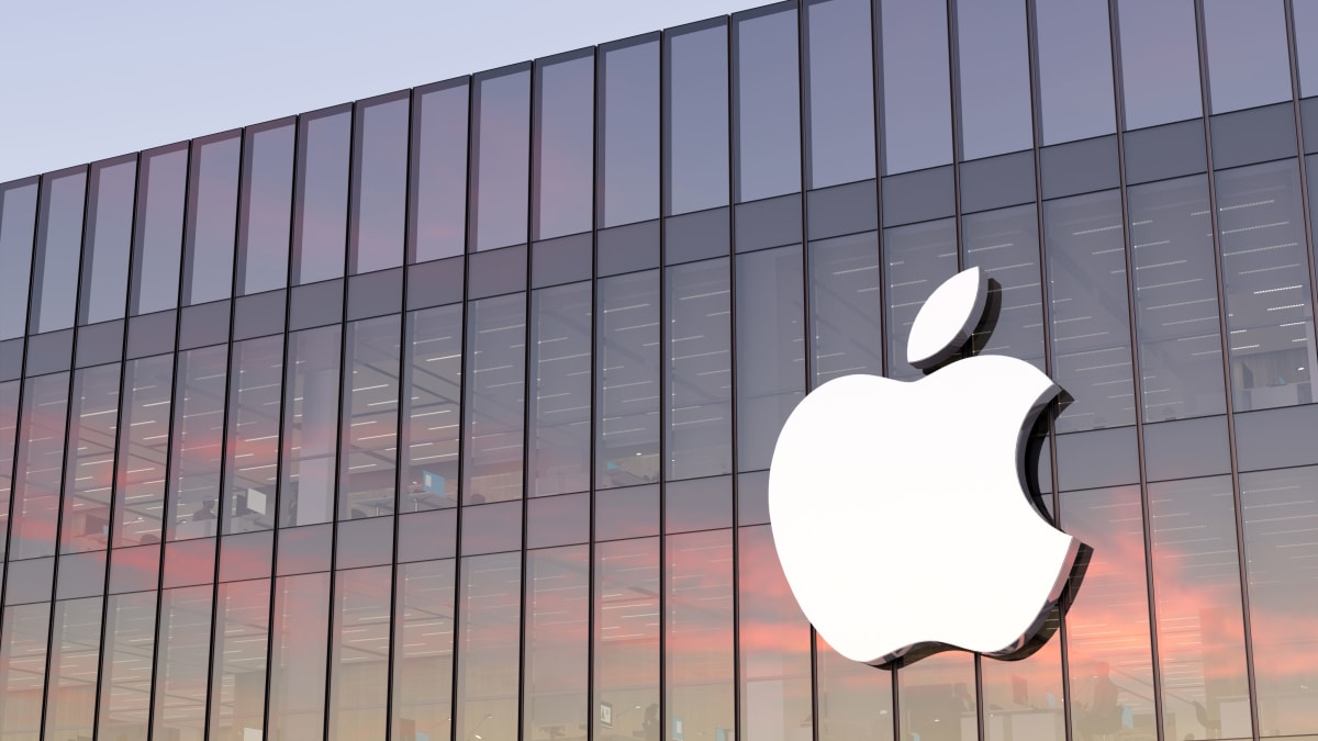 Gün batımında camlı bir Apple binasının cephesindeki büyük beyaz Apple logosu.