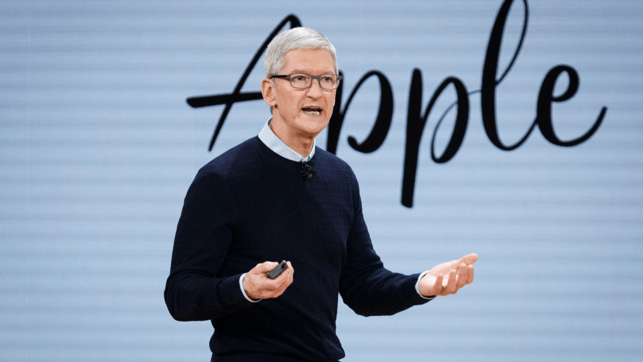 Tim Cook, arkasında el yazısıyla Apple yazan bir perde önünde sahnede konuşuyor.