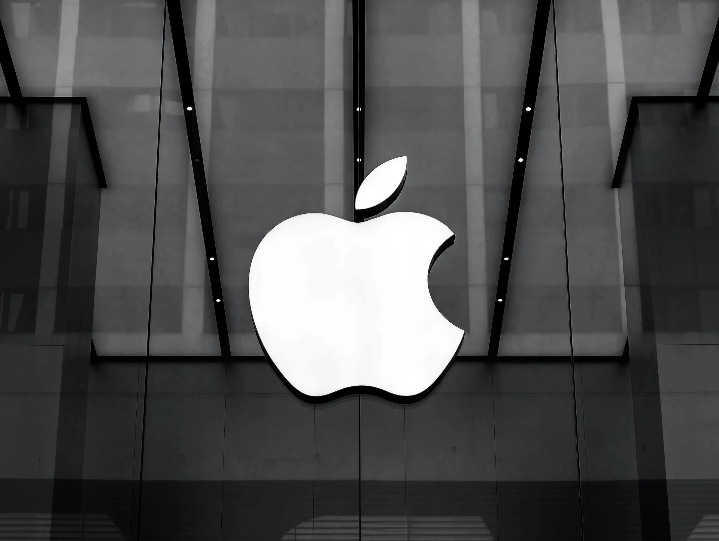 Siyah beyaz fotoğrafta bir Apple mağazasının cam cephesindeki büyük beyaz Apple logosu.